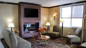 A hotel room with a flat-screen TV mounted on the wall, two armchairs, a sofa, a coffee table, and a patterned carpet. - Comfort Inn Dunmore - Scranton East (Scranton)
