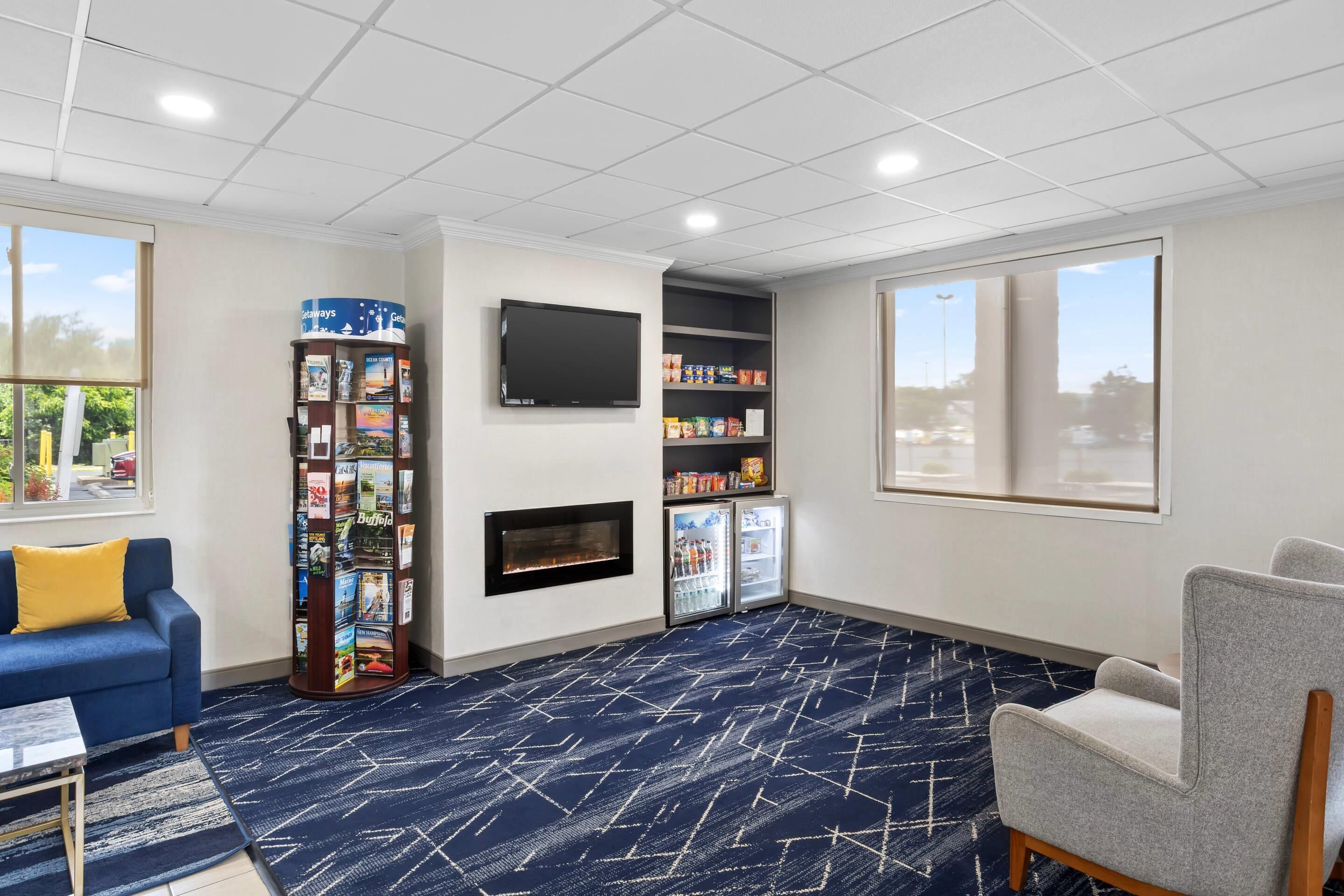 Habitación de hotel con sofá azul, una mesita, chimenea, televisor, estantería y minibar.