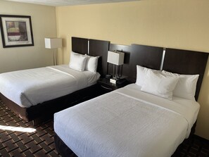 A hotel room with two beds, a nightstand with a lamp, and a framed picture on the wall.