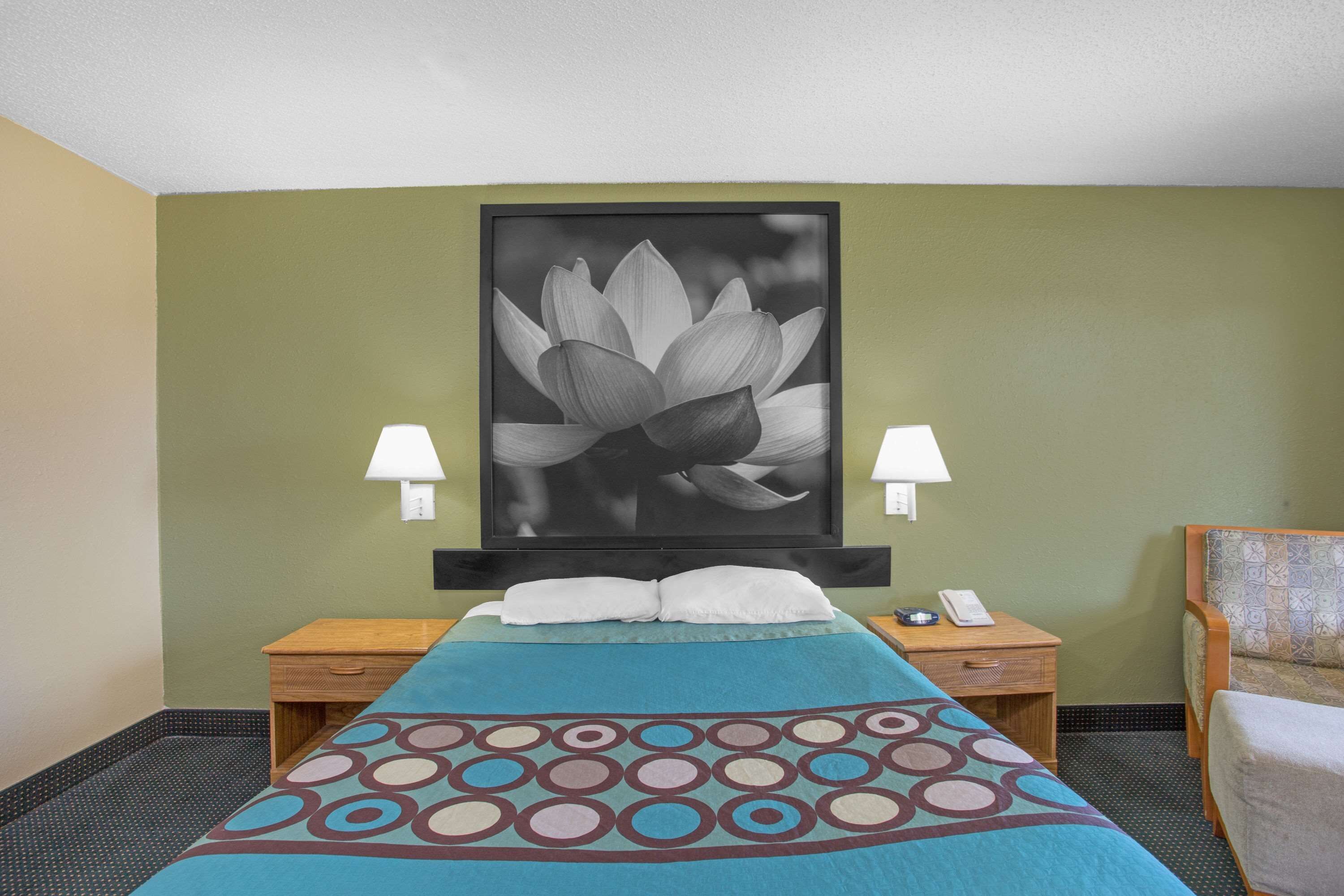 A hotel room with a bed, two bedside tables, a nightstand, a lamp, and a large framed picture on the wall.