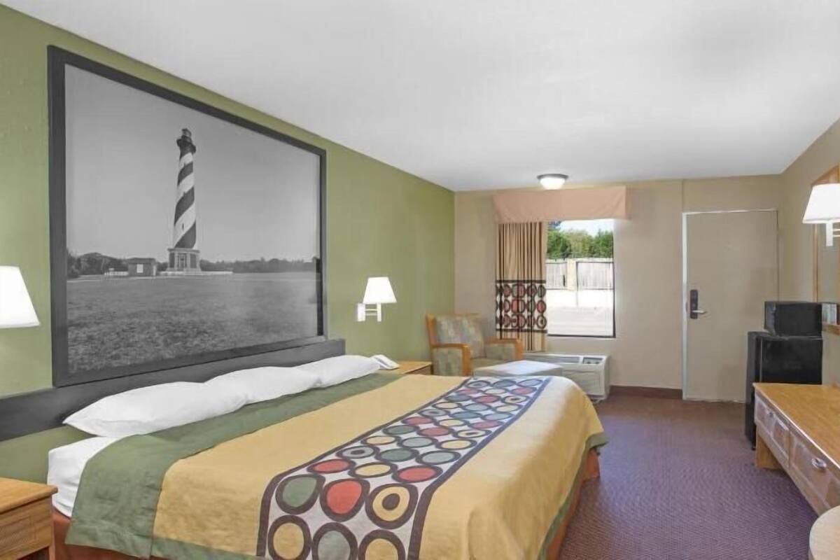 A hotel room with a bed, a desk, a TV, and a painting of a lighthouse.