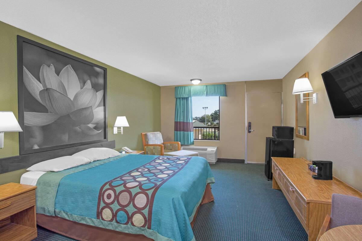 A hotel room with a bed, a desk, a TV, and a large window with a view of the outdoors.