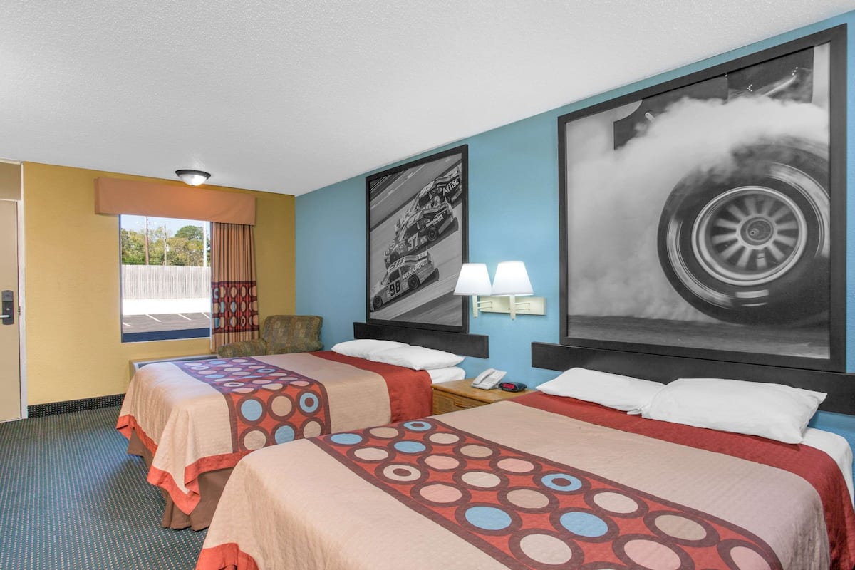 A hotel room with two beds, a window with a view, and a large tire poster on the wall.