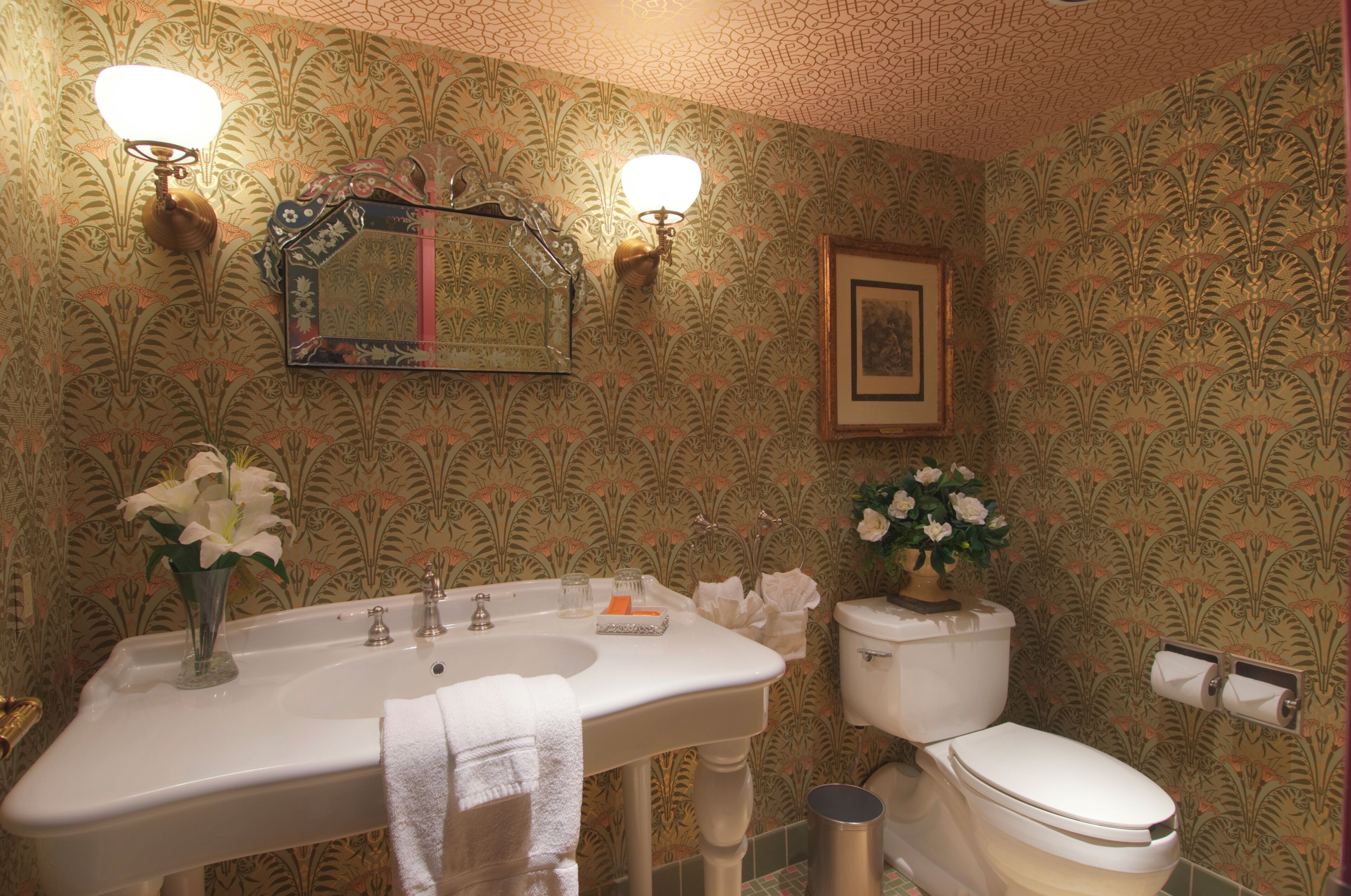 Une salle de bain avec un lavabo, un miroir, des toilettes et un papier peint à motifs.
