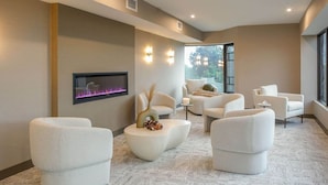 A modern spa room with a fireplace, comfortable seating, and a large window offering a view of the outdoors.