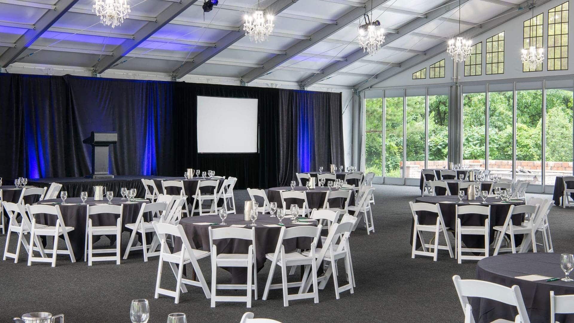 A conference room with tables and chairs, a stage with a screen, and large windows.