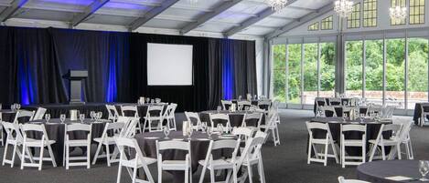 A conference room with tables and chairs, a stage with a screen, and large windows.