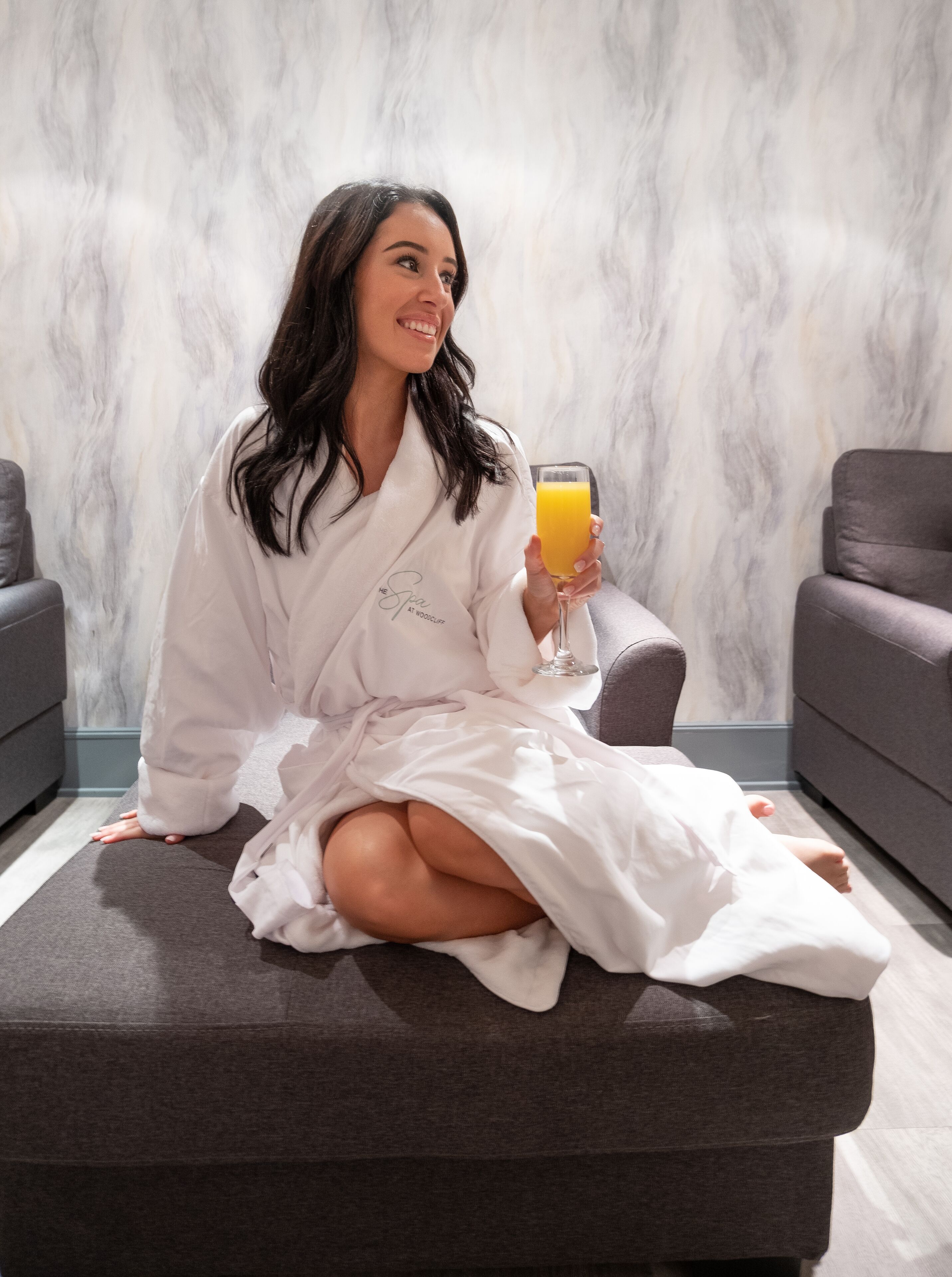A person sitting on a grey ottoman in a room with a marble wall.