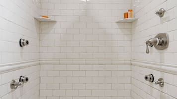Un pequeño box de ducha con azulejos, techo blanco y suelo con estampado verde y blanco, y una sola repisa con artículos de aseo.