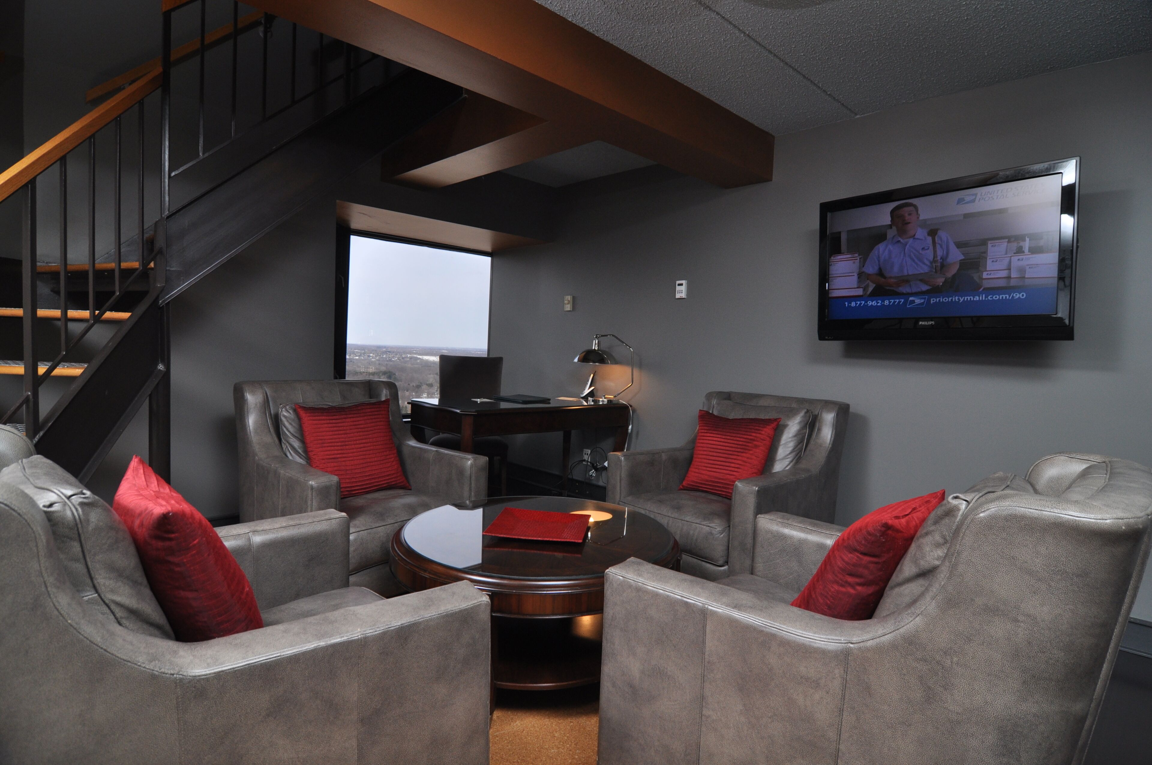 A modern living room with grey sofas, a coffee table, a TV mounted on the wall, and a staircase.