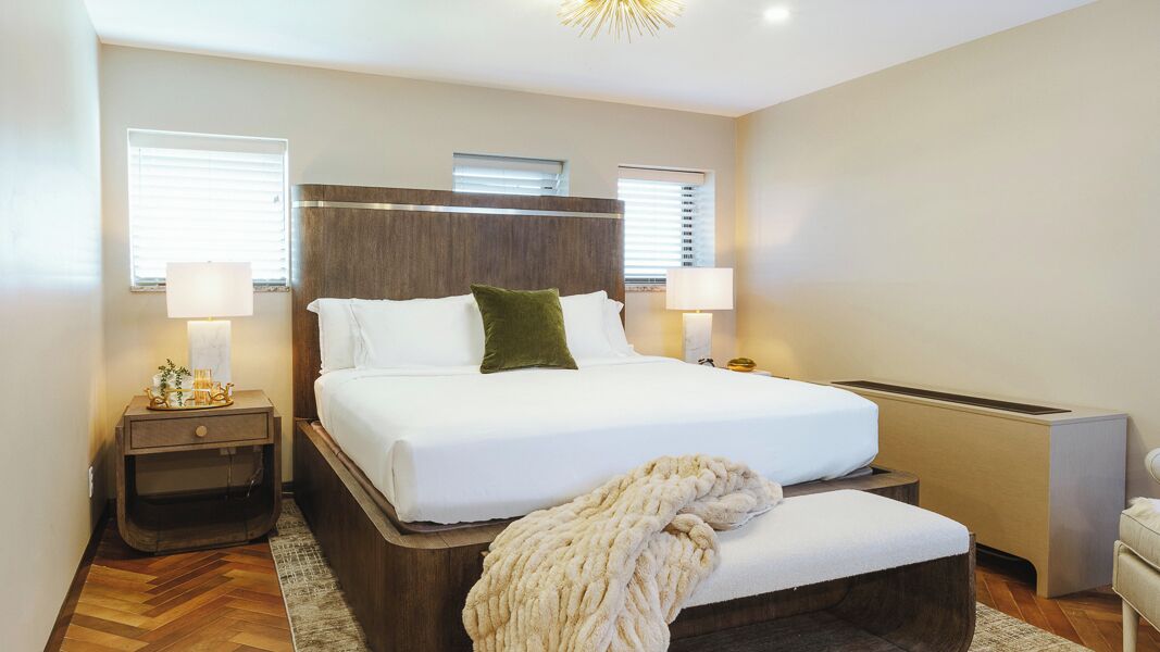 A modern hotel room with a large bed, bedside lamps, a wooden headboard, and a small bedside table.
