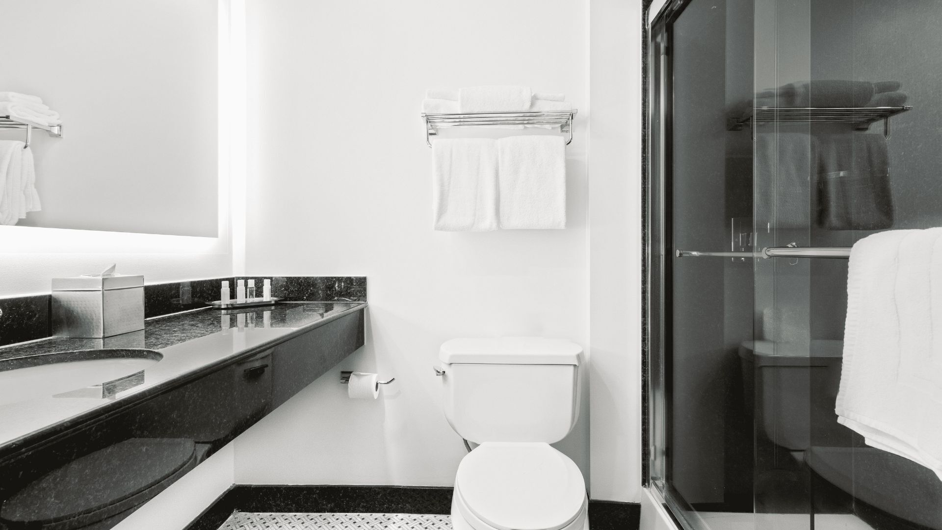 A modern bathroom with a glass shower enclosure, a white toilet, and a marble countertop with a sink and soap dispenser.