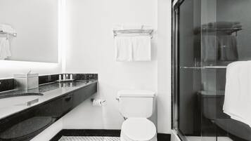 A modern bathroom with a glass shower enclosure, a white toilet, and a marble countertop with a sink and soap dispenser.