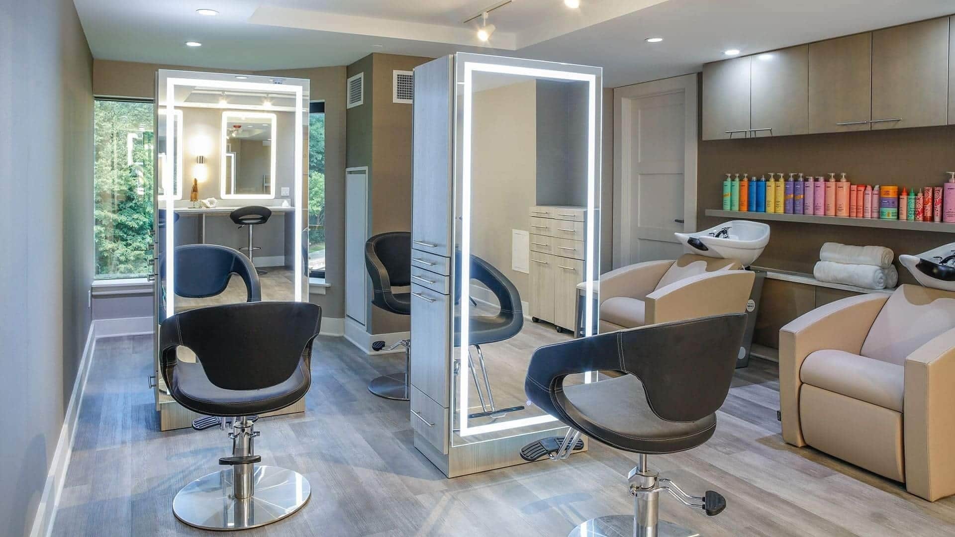 A modern hair salon with two black salon chairs, a large mirror, and a variety of hair products on shelves.