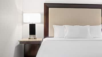 A neatly made bed with white linens and a wooden headboard, a bedside table with a lamp, and a small nightstand.