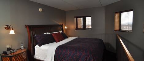 A hotel room with a wooden bed, two bedside lamps, a nightstand, and a window with blinds.