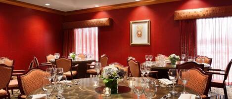 A hotel dining room with round tables, red walls, and classic decor.