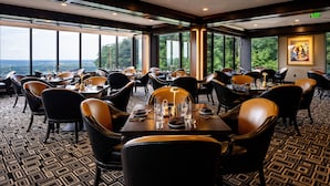 A restaurant with multiple tables and chairs, large windows offering a view of the outdoors, and a patterned carpet.