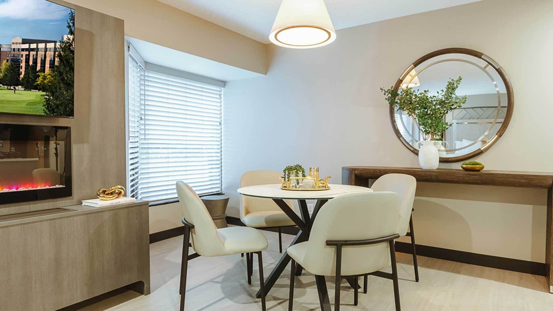 Un espace repas moderne avec une table ronde, quatre chaises, une cheminée et un grand miroir au mur.