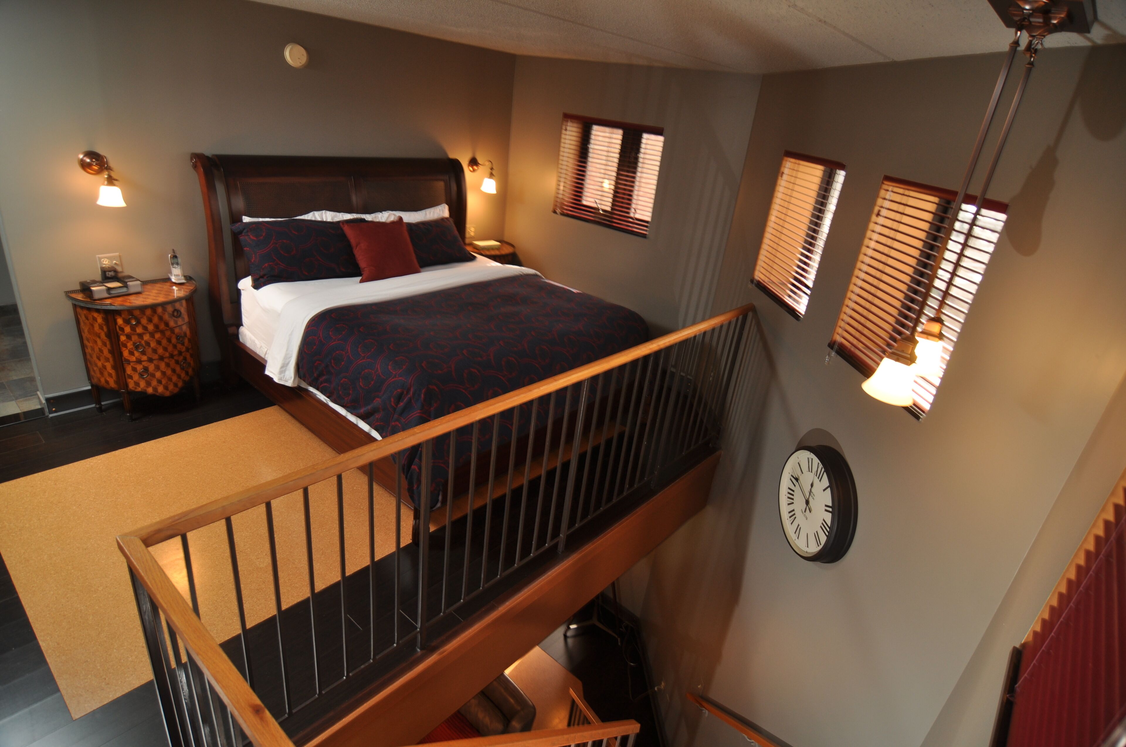 Une chambre à coucher avec un lit, une table de chevet, une horloge murale et un escalier.