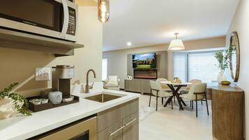 A modern kitchen with a built-in microwave, coffee maker, and sink. There is a dining area with a table and chairs, and a TV mounted on the wall.