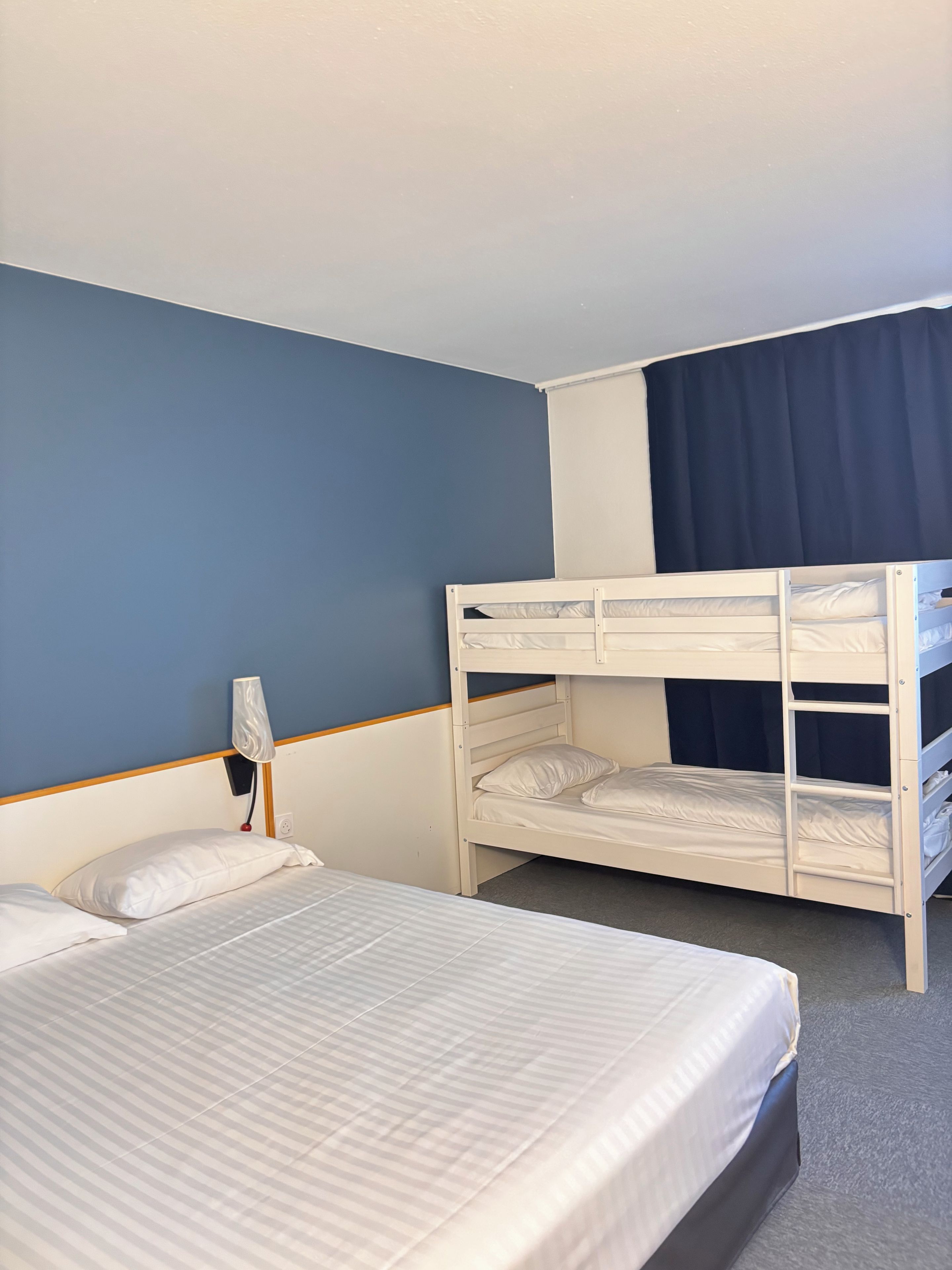 A hotel room with a bunk bed, a single bed, and a lamp.