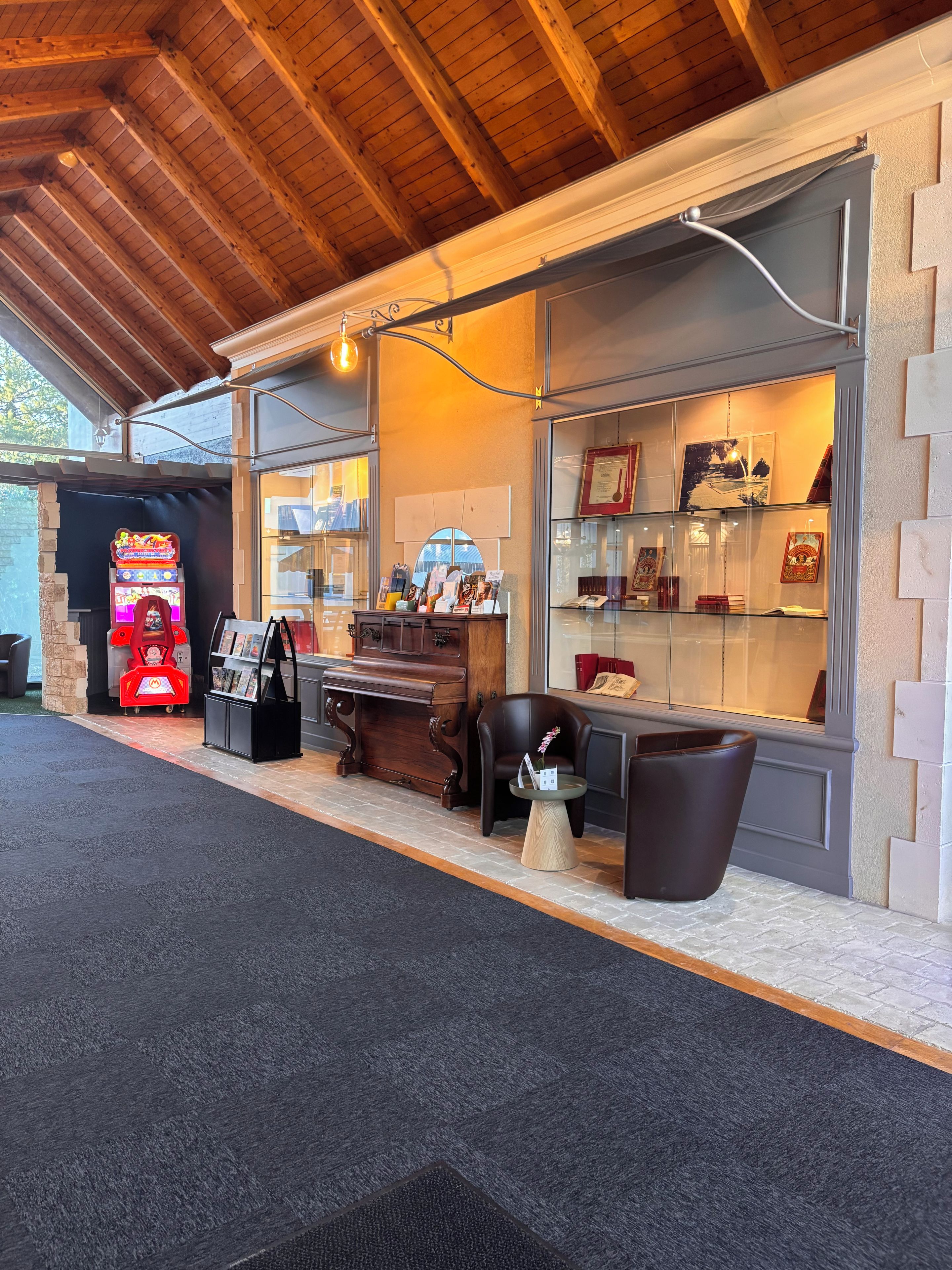 Un espace intérieur chaleureux avec un plafond en bois, un juke-box, un piano et une vitrine où sont exposés des objets encadrés.