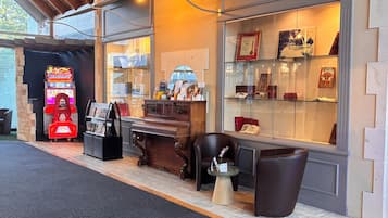 Un espace intérieur chaleureux avec un plafond en bois, un juke-box, un piano et une vitrine où sont exposés des objets encadrés.