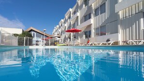 Una piscina con sillas de descanso y sombrillas, rodeada por un edificio con varios balcones.