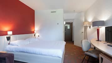 A hotel room with a bed, a desk, and a chair. There is a door leading to another room.
