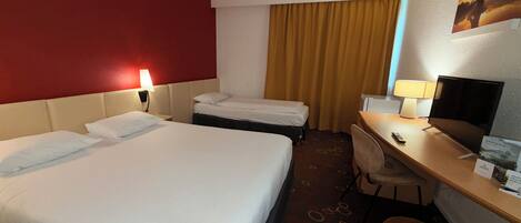 A hotel room with two beds, a desk, a chair, a TV, and a red accent wall.