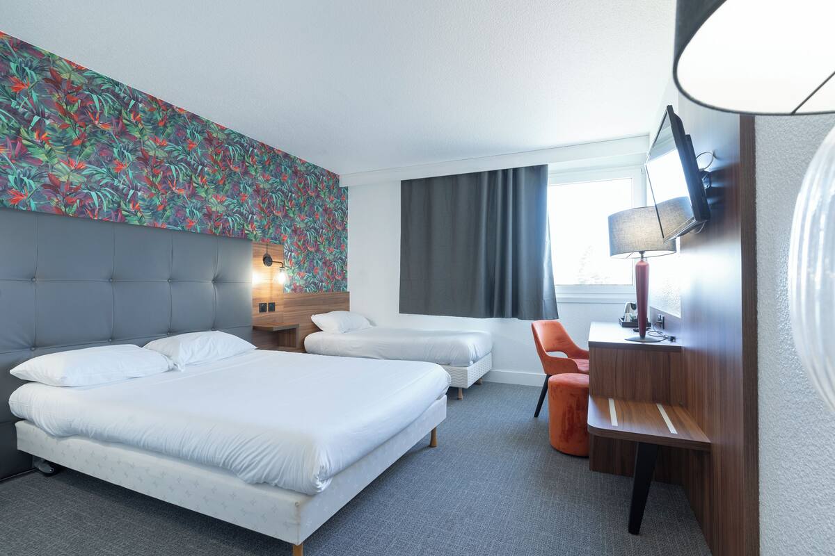 A hotel room with two beds, a desk, a chair, a TV, and a window with curtains.