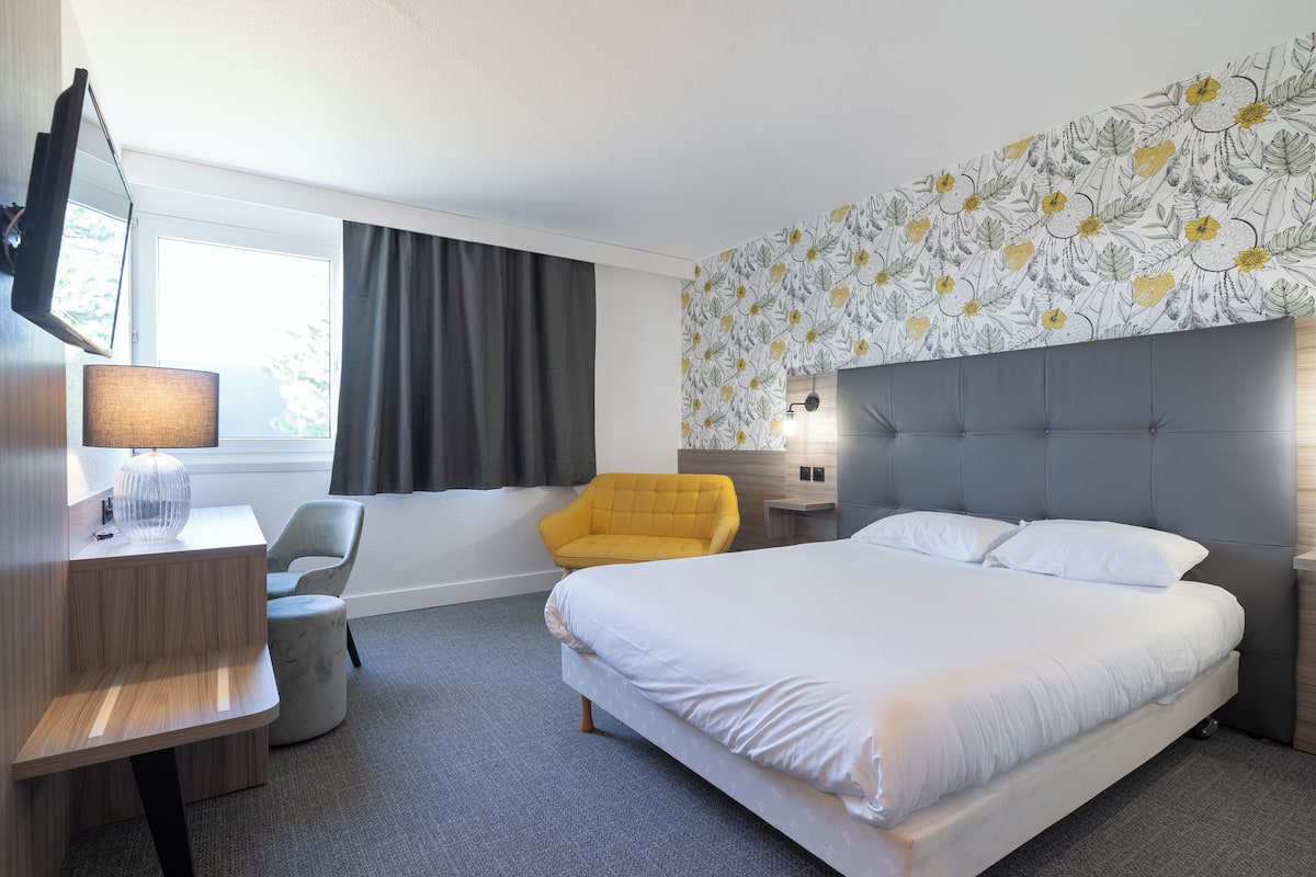 A hotel room with a bed, a desk, a chair, and a large window.