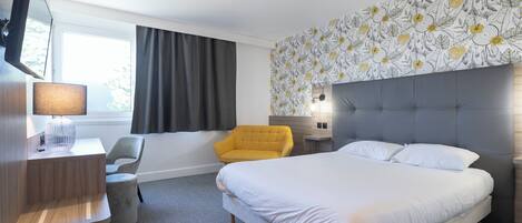 A hotel room with a bed, a desk, a chair, and a large window.