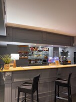 Zona de bar con mostrador, estanterías llenas de botellas y dos sillas de mimbre.
