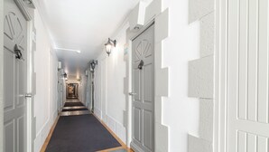 Un pasillo largo y estrecho con puertas blancas a ambos lados, una alfombra oscura y un suelo de tono claro.