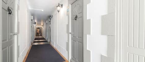 A long, narrow hallway with white doors on both sides, a dark carpet, and a light-colored floor.