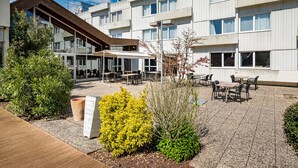Un patio con mesas al aire libre, rodeado por un edificio de diseño moderno y numerosas ventanas.