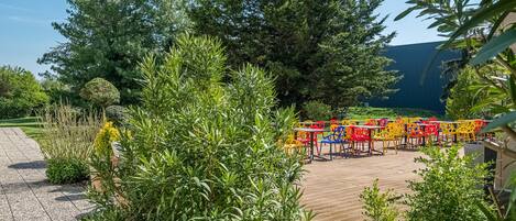 Un espace extérieur aménagé avec des tables et des chaises, entouré de verdure et d’arbres.