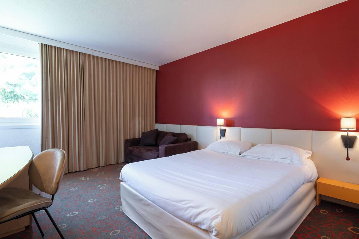 A hotel room with a large bed, a desk, a chair, and a sofa.