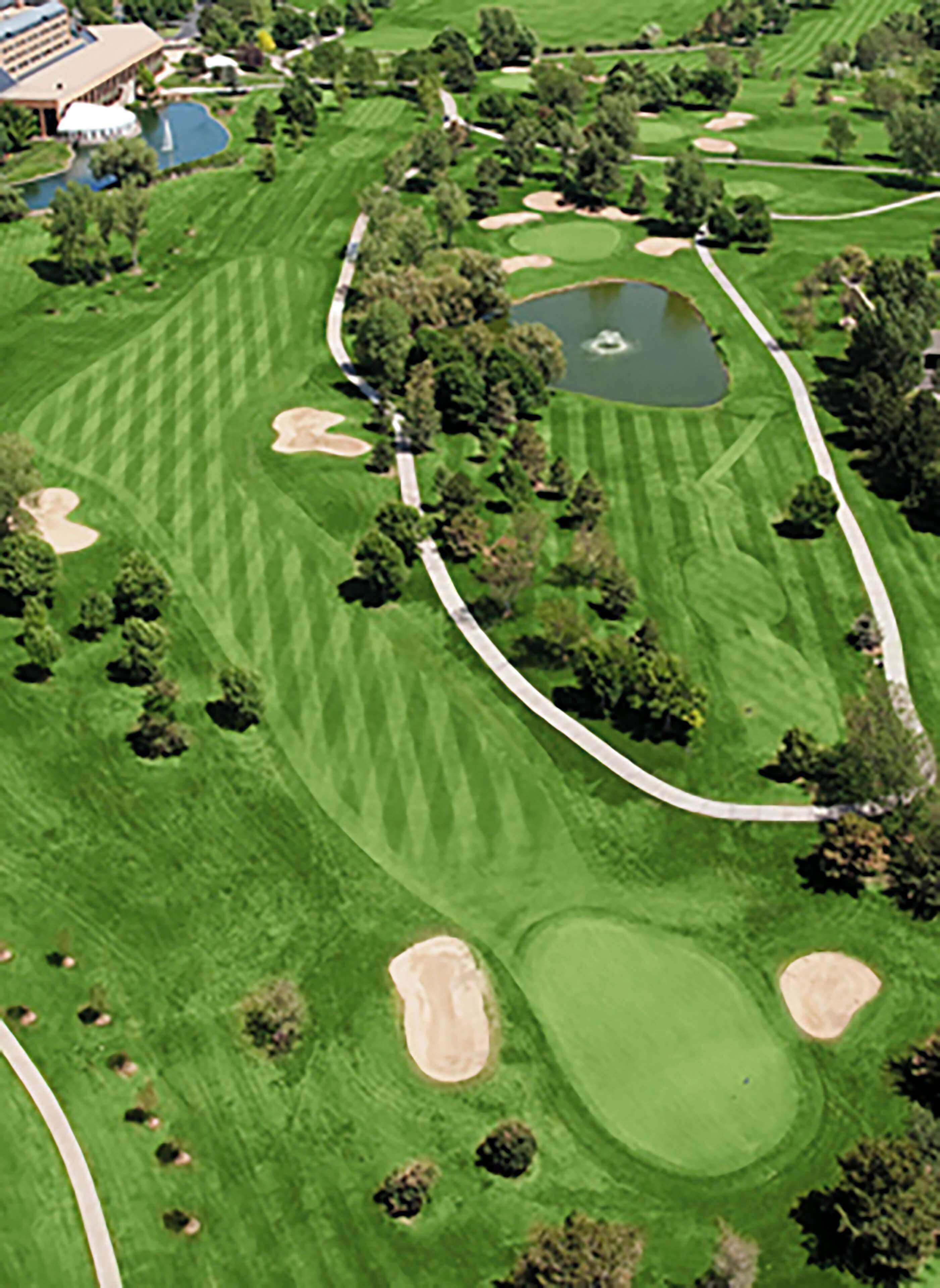 A golf course with bunkers, a pond, and a building with a blue roof.