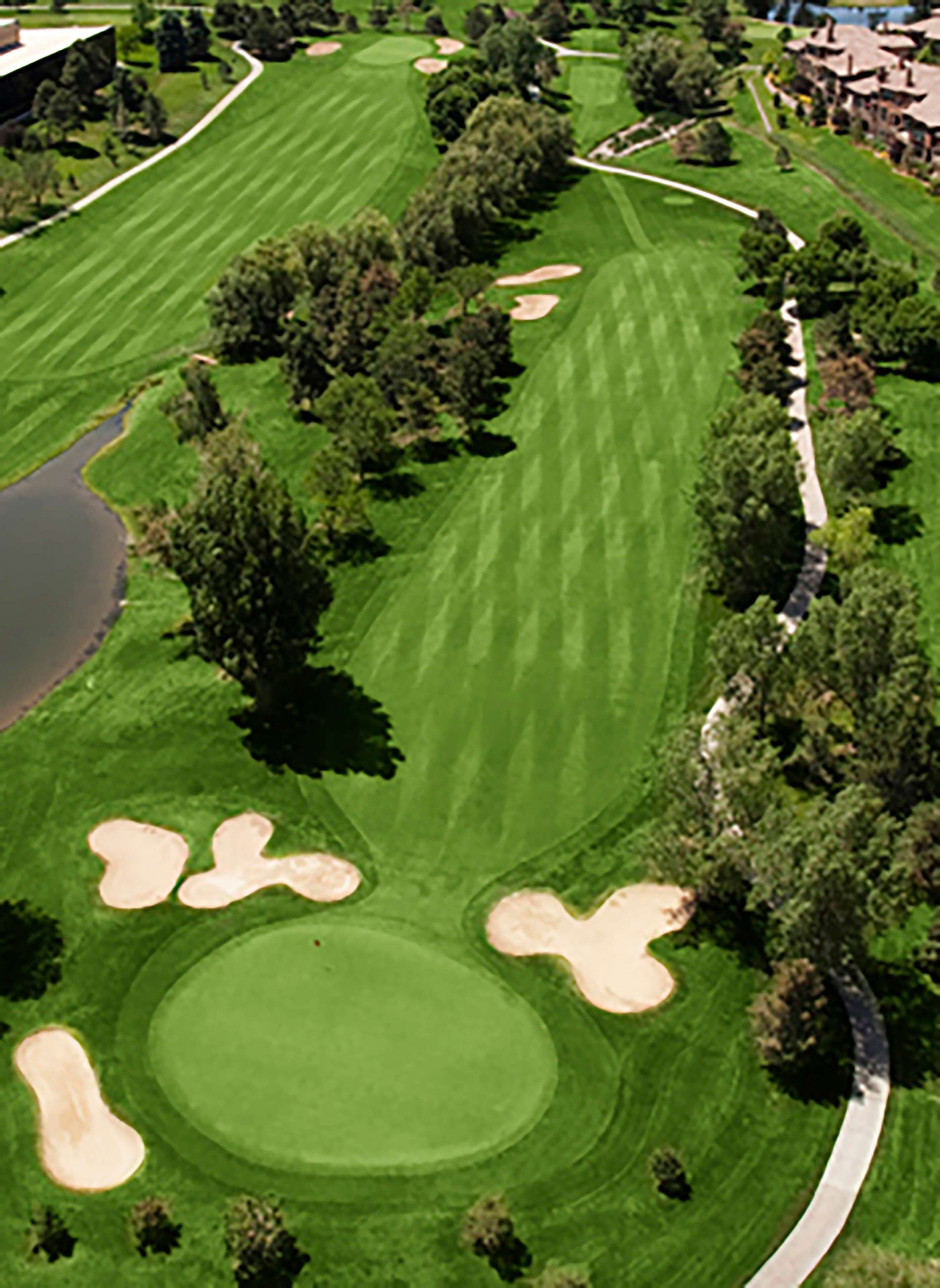 Vista aérea de un campo de golf con bunkers de arena, obstáculos acuáticos y un club de campo.