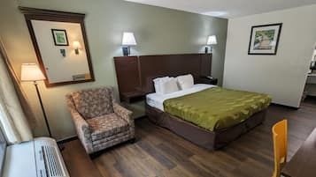 Una habitación de hotel con cama, una silla, una mesita de noche, una lámpara y un cuadro en la pared.