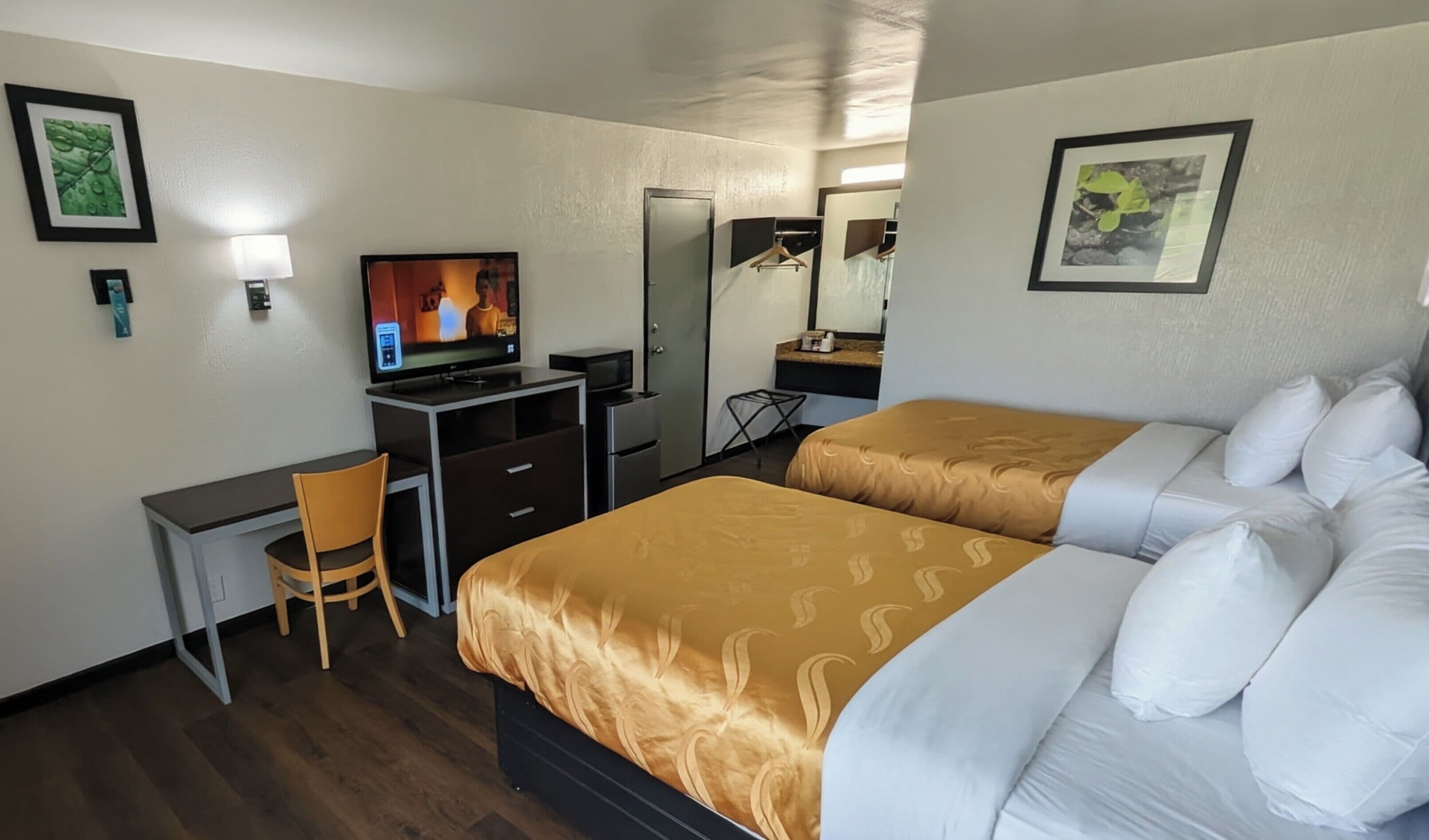A hotel room with two beds, a desk, a television, and a mirror.