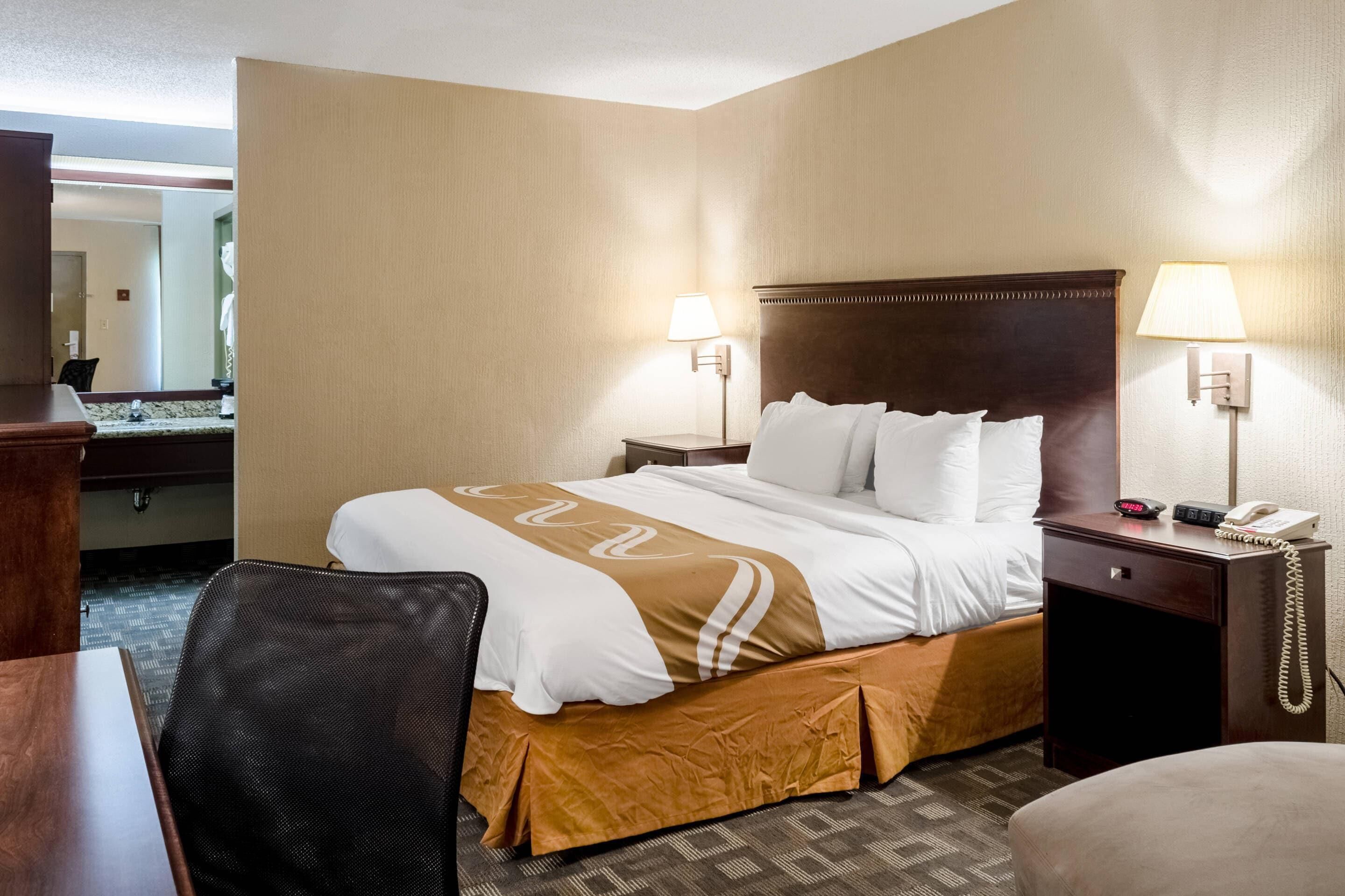A hotel room with a large bed, two bedside tables, a desk, and a chair.