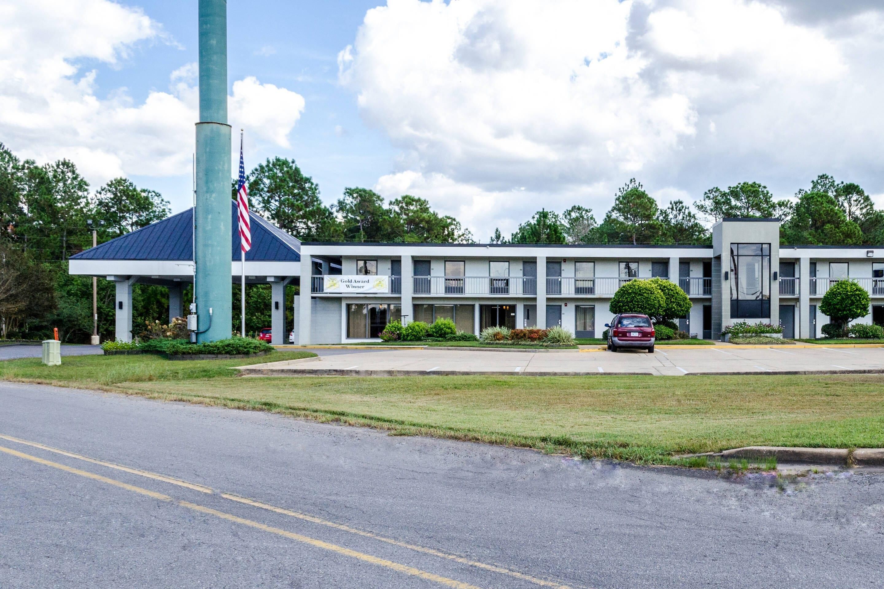 A building with a flagpole, a sign indicating a Gold Award Winner, and a parking lot with cars.
