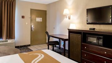 Quarto de hotel com cama, escrivaninha, cadeira, televisão e micro-ondas.