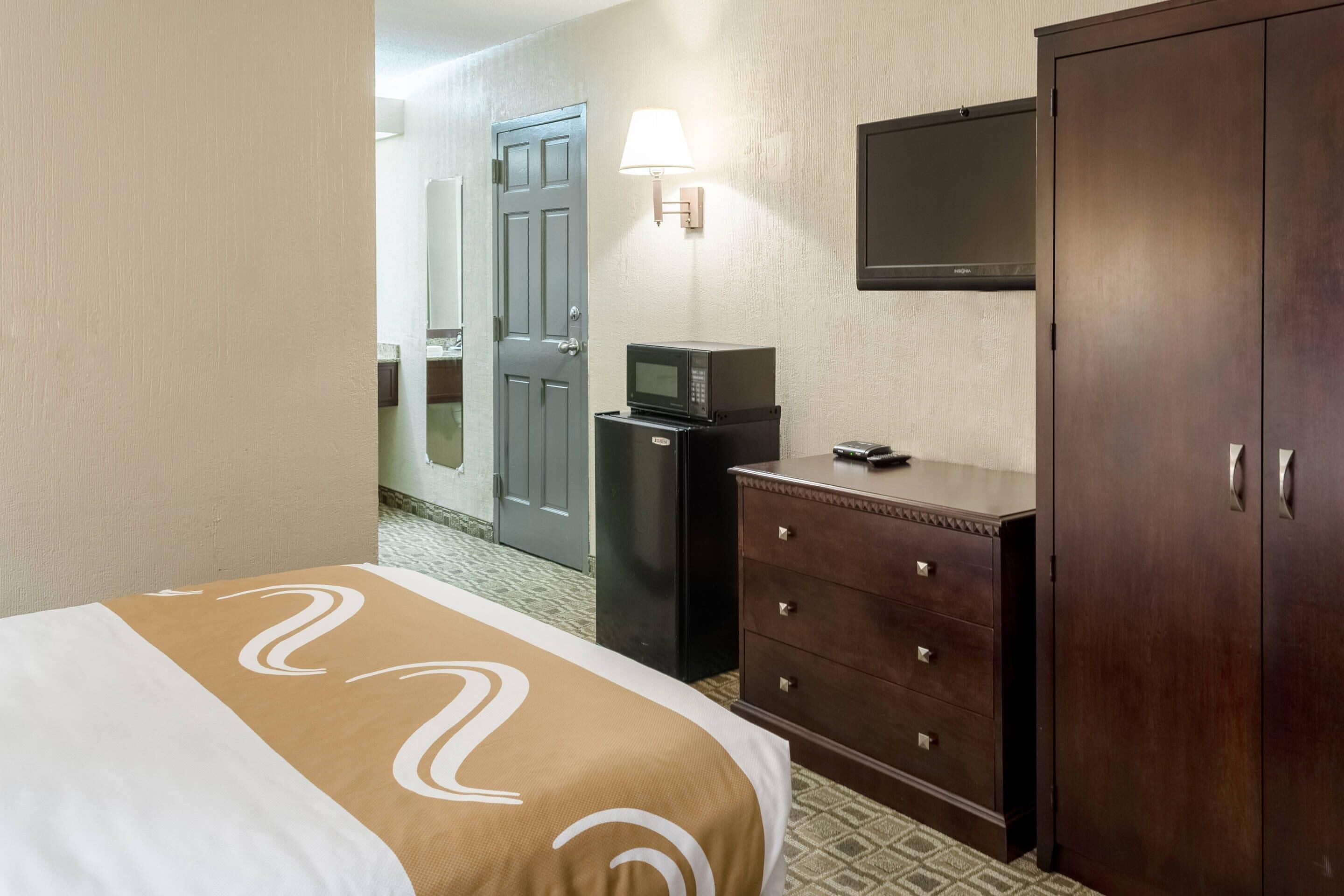 A hotel room with a bed, a dresser, a television mounted on the wall, and a door leading to another room.