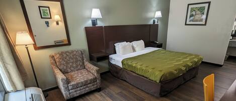 A hotel room with a bed, a chair, a nightstand, a lamp, a picture on the wall, and a window.