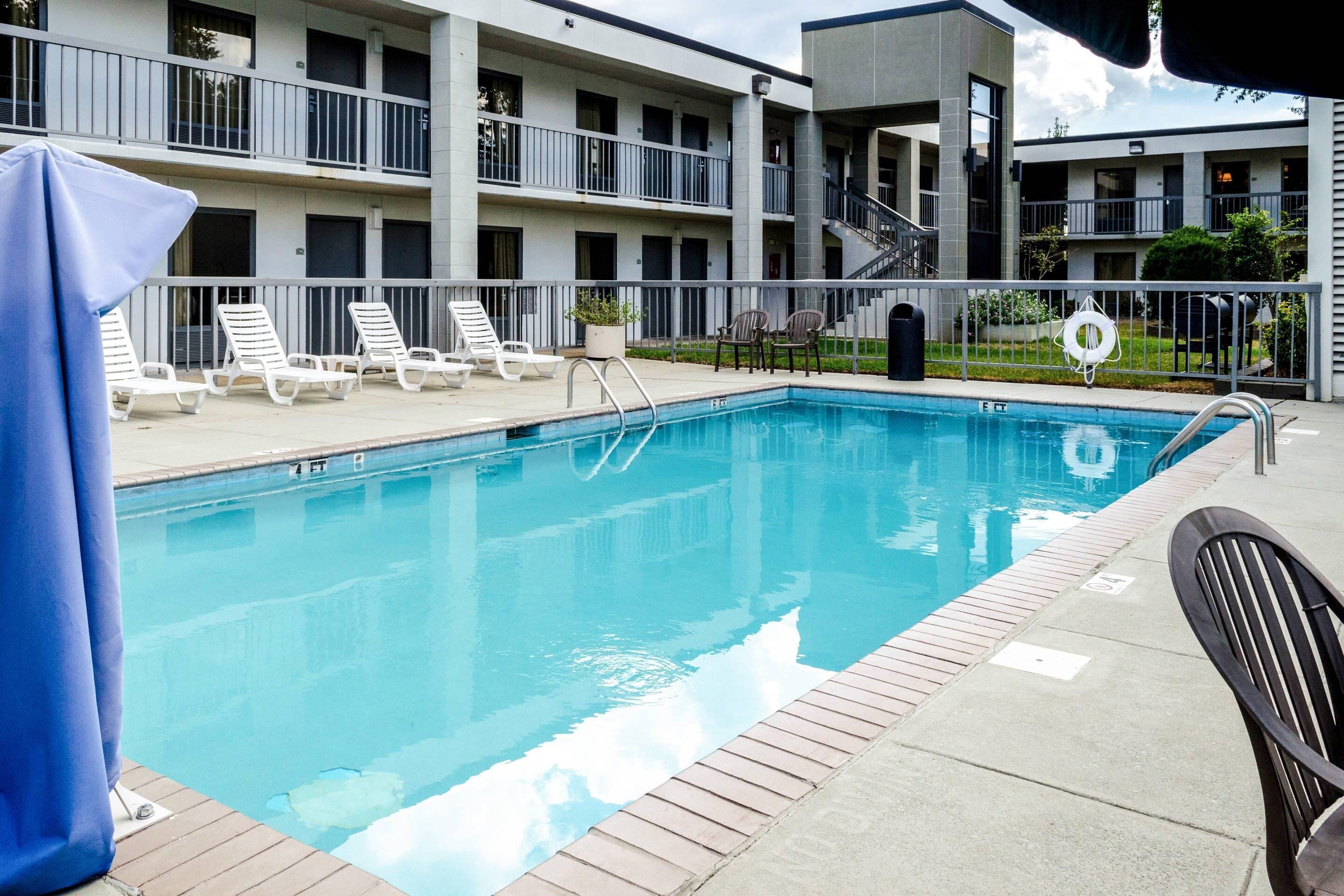 A swimming pool with lounge chairs and a covered area, surrounded by a multi-story building with balconies.